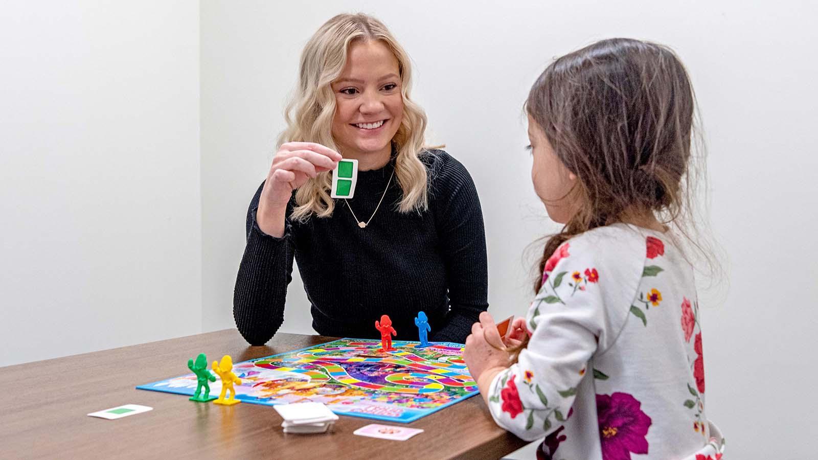 College student playing board game with young girl